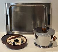 Photo of full lot showing the ice bucket with lid, barware kit in open round case, and stainless steel rectangular serving tray with black handles behind.