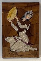 Front view of rectangular mother-of-pearl inlaid wood panel depicting a kneeling woman playing a frame drum