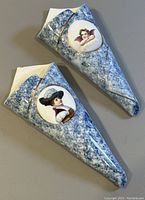 Two cone-shaped porcelain wall vases with blue speckled exterior, one featuring a woman portrait, the other a cherub angel portrait with gold trim.