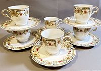 Full set of six demitasse cups and matching saucers showing floral and scroll design in orange, green, and blue with gold trim.