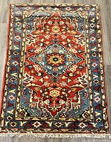 Front full view of the vintage Persian handwoven wool rug showing the central medallion and border designs in red, blue, cream and yellow colors.
