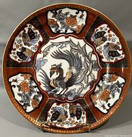 Front view of vintage 10.5-inch Saji Japanese decorative plate with central phoenix and surrounding floral and butterfly designs in gold, black, orange, and blue.
