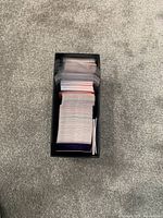 Top-down view of a large stack of Disney themed cards contained in a black rectangular box on a grey carpet.