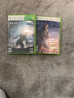 Photo showing two Xbox 360 game cases: Halo 4 and Halo 3 with visible cover art on carpeted floor.