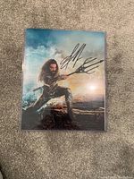Glossy color photograph of Jason Momoa as Aquaman holding a trident with a visible autograph in black ink.