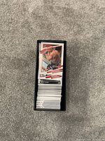Stack of mixed sports trading cards in a black cardholder box with a visible front card featuring a boxer in action, including logos and player stats.