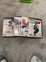 Five NHL sports video games for PlayStation 2 and Xbox 360 arranged fanned out on carpeted floor.