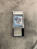 Top view of a BGS 10 graded Lapras V Pokémon card in a protective case sitting atop a box containing numerous other ungraded Pokémon cards.