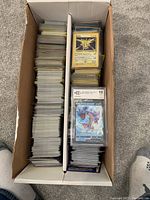Top-down view of white cardboard organizer box filled with sleeved and unsleeved Pokemon cards in two compartments