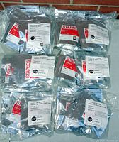 Lot of 24 individually foil-packaged Staples remanufactured Canon CL-241XL ink cartridges arranged in four rows against a brick background.