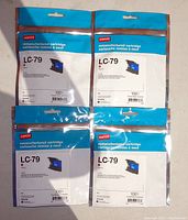 Photo showing 4 remanufactured Staples LC79 magenta ink cartridges in sealed packaging, arranged in a 2x2 grid on a neutral surface.