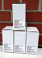 Photo of four boxed Lexmark cyan toner cartridges stacked in front of a brick wall. Boxes show part numbers C544X2CG and C544X1CG with label NUPC544C.