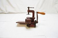 Front and side view of vintage red metal pinking machine with wooden handle, showing blade and clamp area.