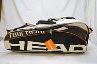 Full side view of the HEAD Tour Team SuperCombi tennis racquet bag showing black and white color scheme with orange accent and large logos, tag still attached.