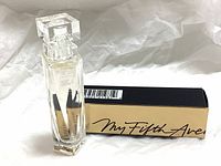 Clear glass perfume bottle with faceted design next to golden box with black script.