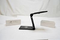 Full view of the black metal flex pan tilt camera mount accessory plate with packaging boxes in the background.