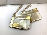 Two metallic patchwork mini pouches in silver and gold laid flat showing front design and wrist straps.