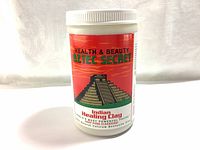 Front view of sealed white plastic container with red and green label showing brand and product name Aztec Secret Indian Healing Clay.
