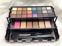 Open collectible tin showing all makeup pieces arranged in three fold-out sections with the top section holding 20 eyeshadows in multiple colors, middle section holding 6 bronzers and highlighters, and bottom section containing two brushes.