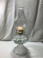 Front view of vintage clear glass oil lamp lit to show wick and burner function