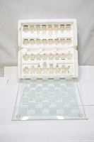Photo showing the full set of clear and frosted glass chess pieces arranged in original white foam holder with the chess board beneath.