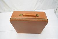 Front view of vintage hard case showing tan leather exterior and handle with brass hardware.