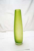 Side view of tall, matte light green vase with vertical texture standing on white surface with a white backdrop.