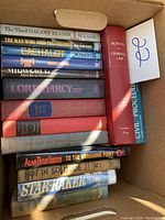 Photo showing a box with a variety of 16 hardcover books stacked and arranged in two layers, including sci-fi novels, legal texts, and other literature.