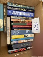 Photo of 17 hardcover books in a box with varying titles and subjects.