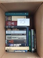 Photo of 13 hardcover books in a cardboard box showing titles and condition
