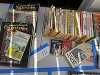 Top down image displaying multiple vintage paperback books arranged on a table including Doonesbury's Greatest Hits volumes boxed set, several National Lampoon magazines, and other paperback books.