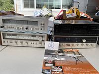 Four audio components on table: two silver-faced tuners stacked on left, black Sony dual cassette deck on right top, silver-faced stereo amplifier/receiver on right bottom.