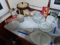 Photo showing vintage Corningware assortment, including dishes with lids and crockpot, small kitchenware and glass bowl.
