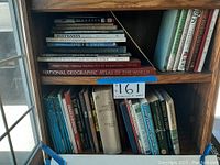 Bookshelf containing a variety of hardcover books focusing on different subjects: elephants, art, military, geography, nature, and encyclopedias. Books vary in size and color, arranged standing and stacked.