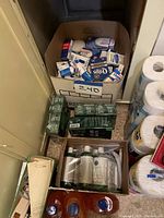 Photo showing a cardboard box filled with multiple bars of Dial soap, green boxed items, bottles of liquid hand soap, and stacked toilet paper rolls.