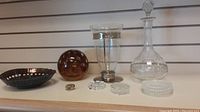 Full shelf lineup showing the glass decanter with stopper, glass vase with metallic accents, large amber bubble glass ball, metal decorative bowl, and small glass items including paperweights and a small ridged bowl.