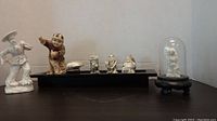 Front view of all the porcelain Asian figurines and carved bird under glass dome on a wooden base