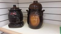 Both brown ceramic cookie jars together on shelf, showing relative size and design details