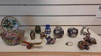 Overview of all cloisonné items on shelf: bowl, plate on stand, vases, trinket boxes and figurines