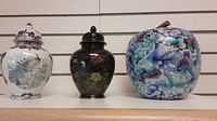 Front view of three cloisonné vases with lids showing various colors and floral designs.