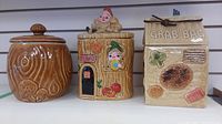 Photo showing all three cookie jars side by side: log style, bakery house with gnomes, and milk carton 'GRAB BAG' style