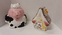 Front view of combined cow and pig cookie jar with chicken lid, and front of house-shaped cookie jar with animal decorations.
