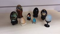 Full lot of eight decorative and stone eggs on stands, various styles and colors