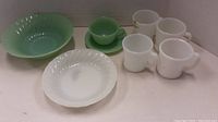 Collection of four white mugs, green bowl, white plate, green cup and saucer placed together.