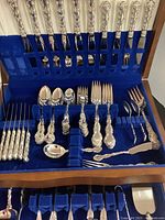 Wooden flatware chest open showing lid rack of 10 dinner knives, slots below for forks and spoons, and tray of serving pieces.
