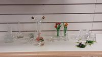 Overview of all assorted glass items including flower bouquets, animal figurines, candlestick holder, glass vessel with corked tubes, and decorative glass apple.