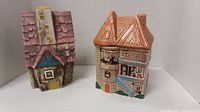 Two house shaped cookie jars placed side by side on a white surface showing front and side views