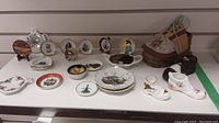 Miniature decor plates and pottery shoes displayed on white surface, showing variety of plates with designs and pottery shoe figures