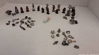 Overall collection of miniature metal figures and charms arranged on a plain surface showing variety of items including a small baby figure and multiple standing small figurines.