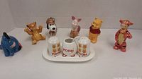Wide shot of all figurines and the Pooh salt and pepper set on a white surface against a white background.